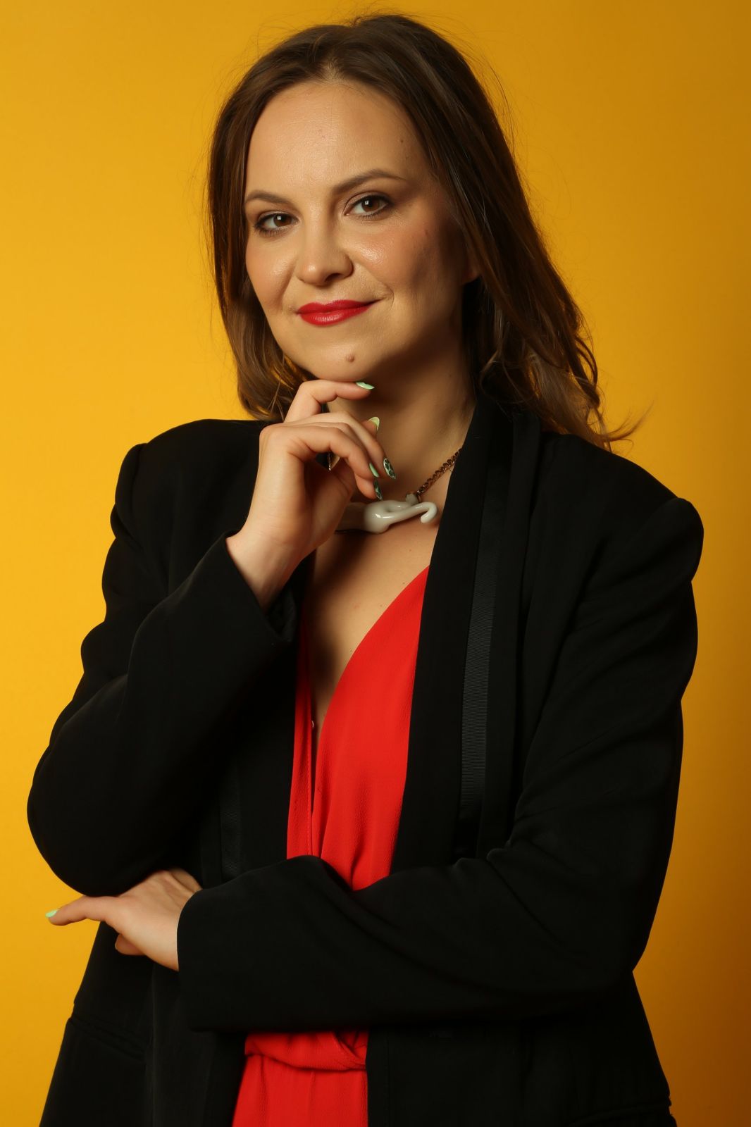 Karina Abramova in a black blazer against a saffron backdrop, hand at her chin